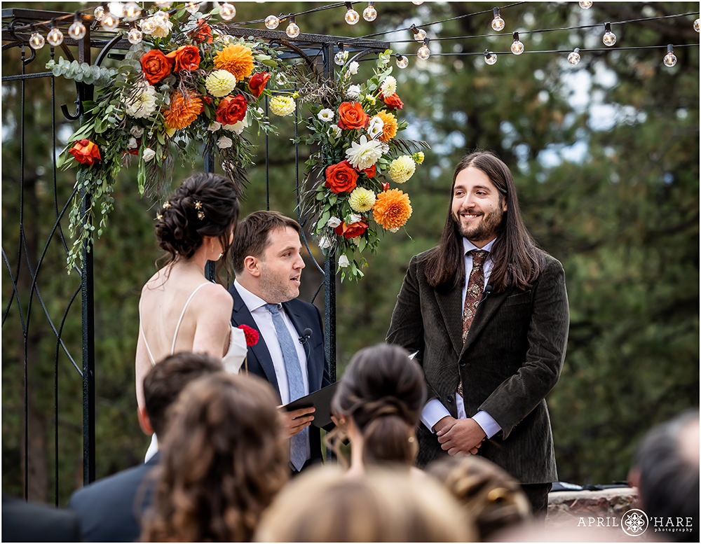 Groom smiles at his bride under the orange florals and string lights of Boettcher Mansion in Colorado