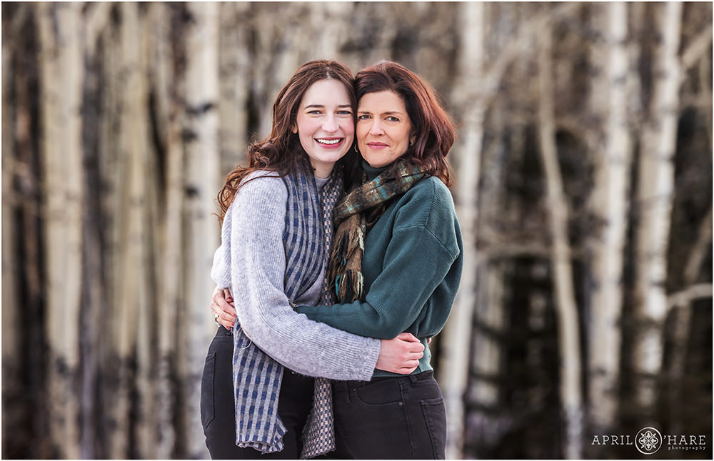 A mom with her adult daughter pose together with a pretty aspen tree backdrop during winter in Colorado