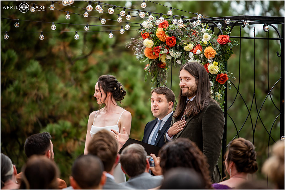 Bride and groom look out at their guests under the orange floral decor of their Boettcher Mansion wedding ceremony