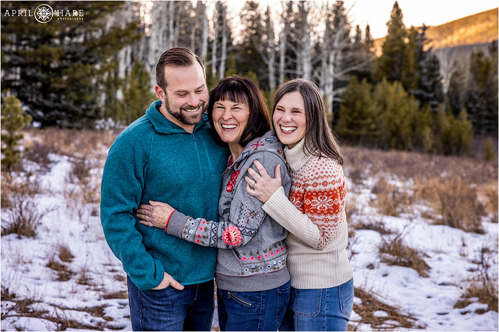 Cute candid family photo of a mom with her two adult children standing in a pretty mountain meadow with snow on the ground in Colorado
