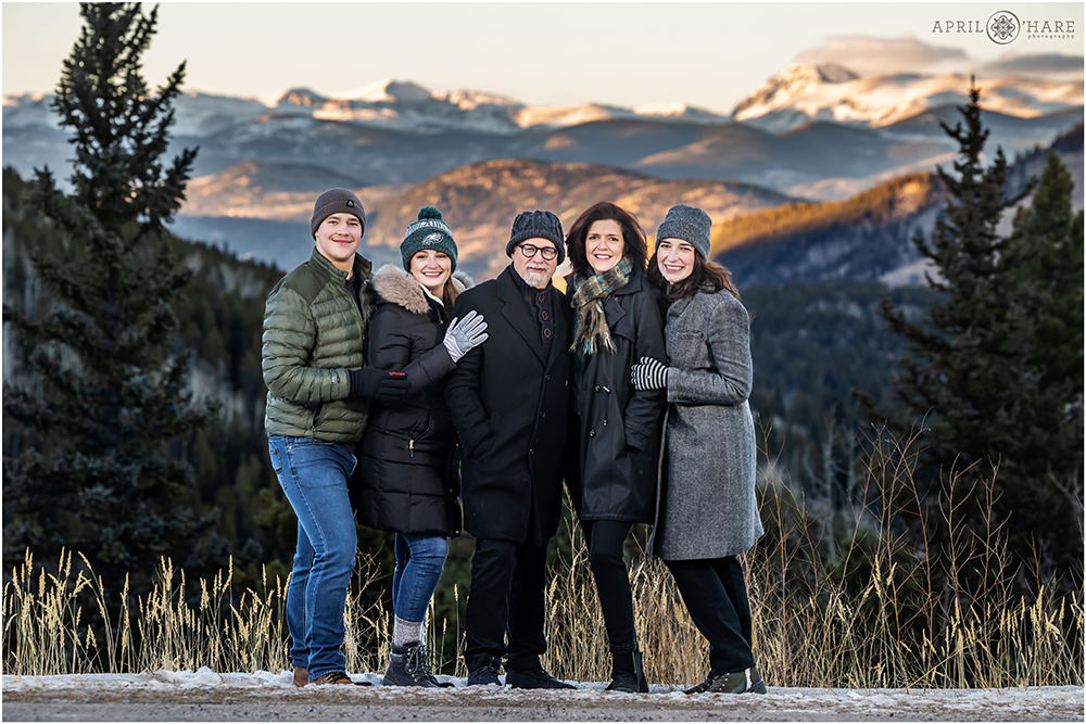 Family all bundled up in their winter gear pose for a portrait together with a pretty mountain backdrop in Evergreen Colorado