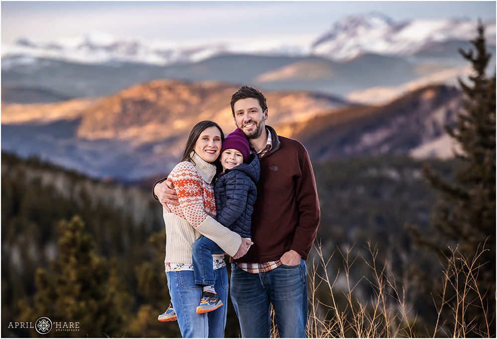 Family of 3 with a cute young son held in their arms on Squaw Pass Road with a mountain backdrop in Colorado
