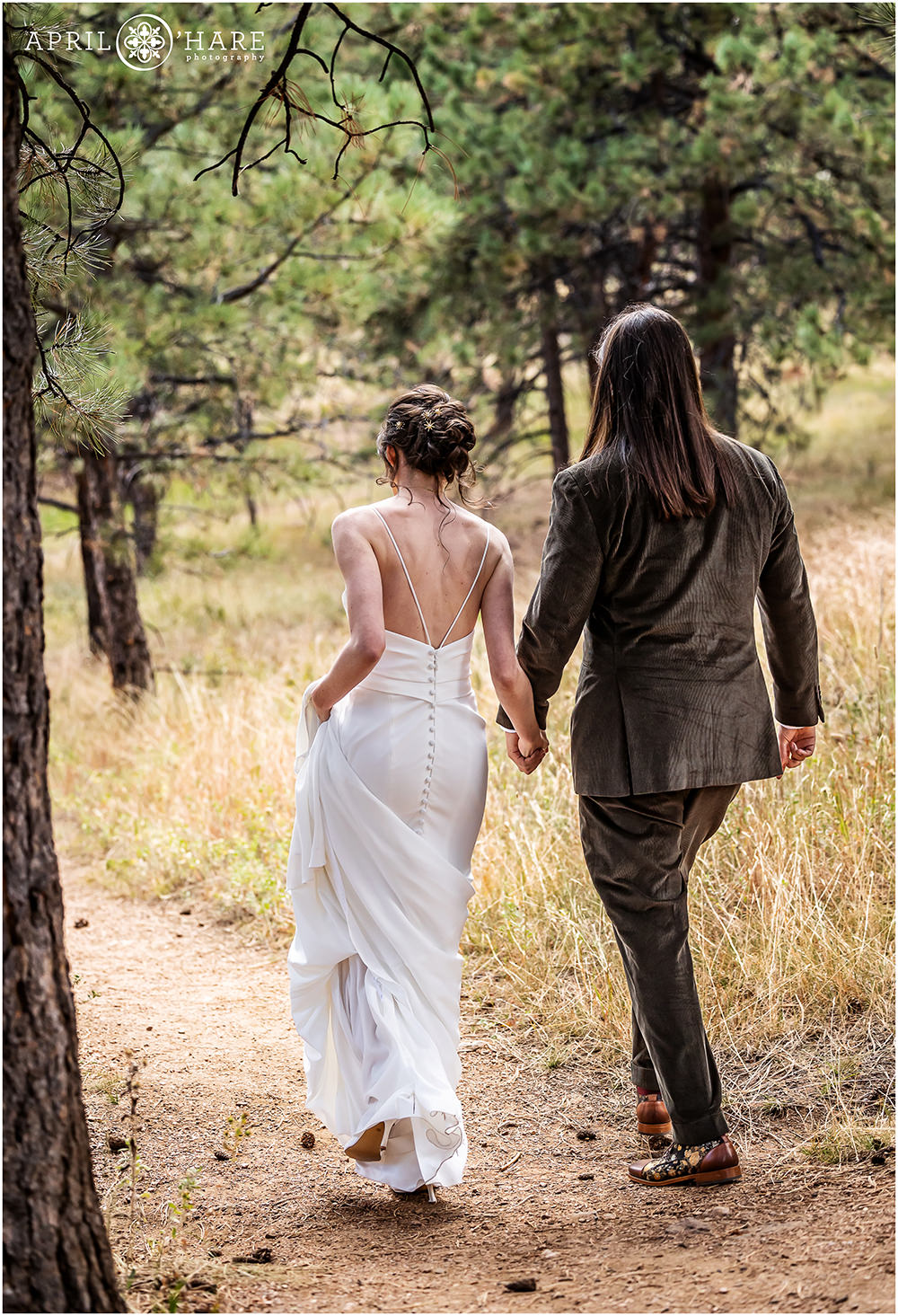 Bride and groom walk to their wedding ceremony in the woods on their Boettcher Mansion wedding day in Colorado