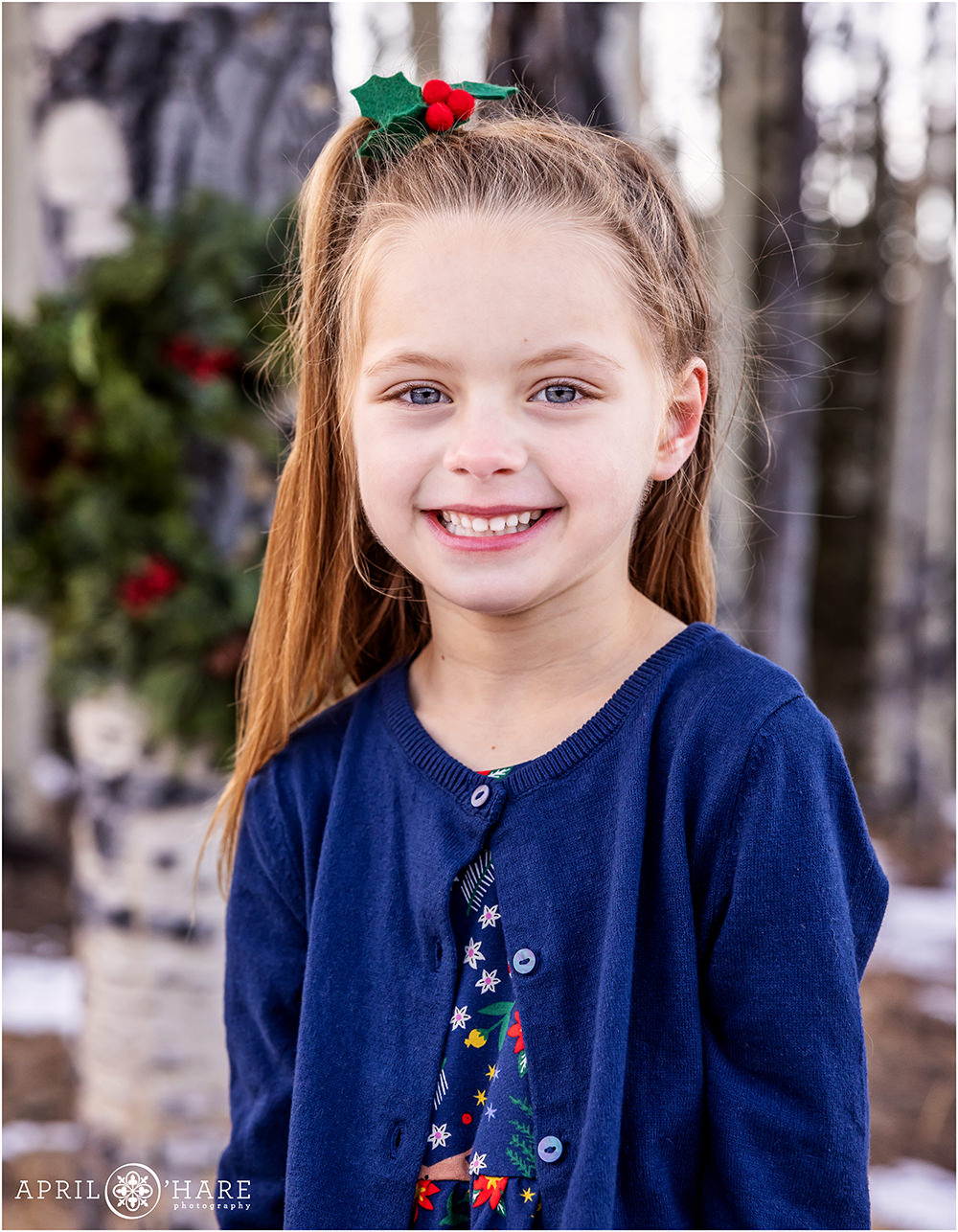 Sweet 5 year old girl Christmas portrait with a wreath hanging on an aspen tree behind her in Colorado