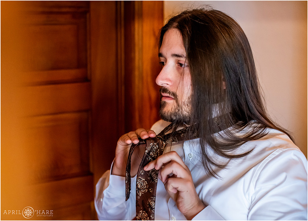 Groom with long hair ties his brown floral tie on his wedding day in Golden CO