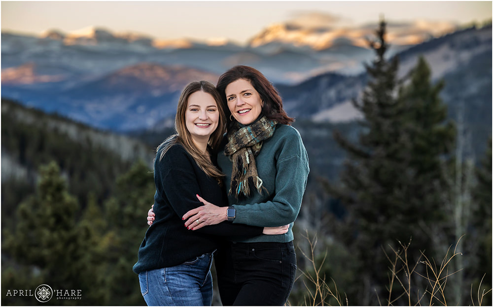 A mom with her daughter pose for a portrait in front of a pretty mountain view during winter