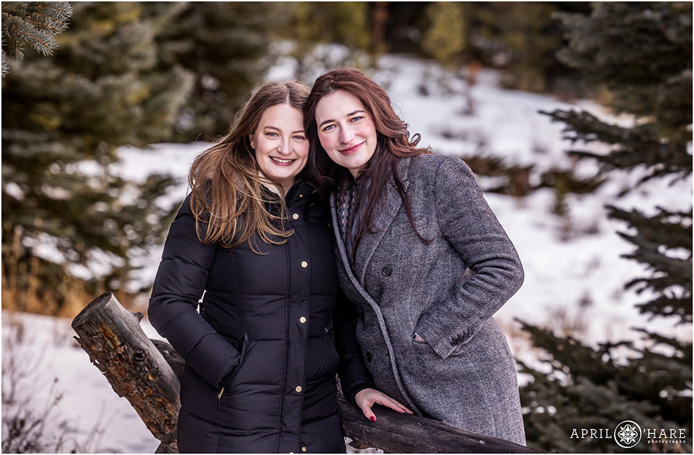 Two pretty sisters wearing coats pose for a photo together in the cold snowy outdoors of Colorado during winter