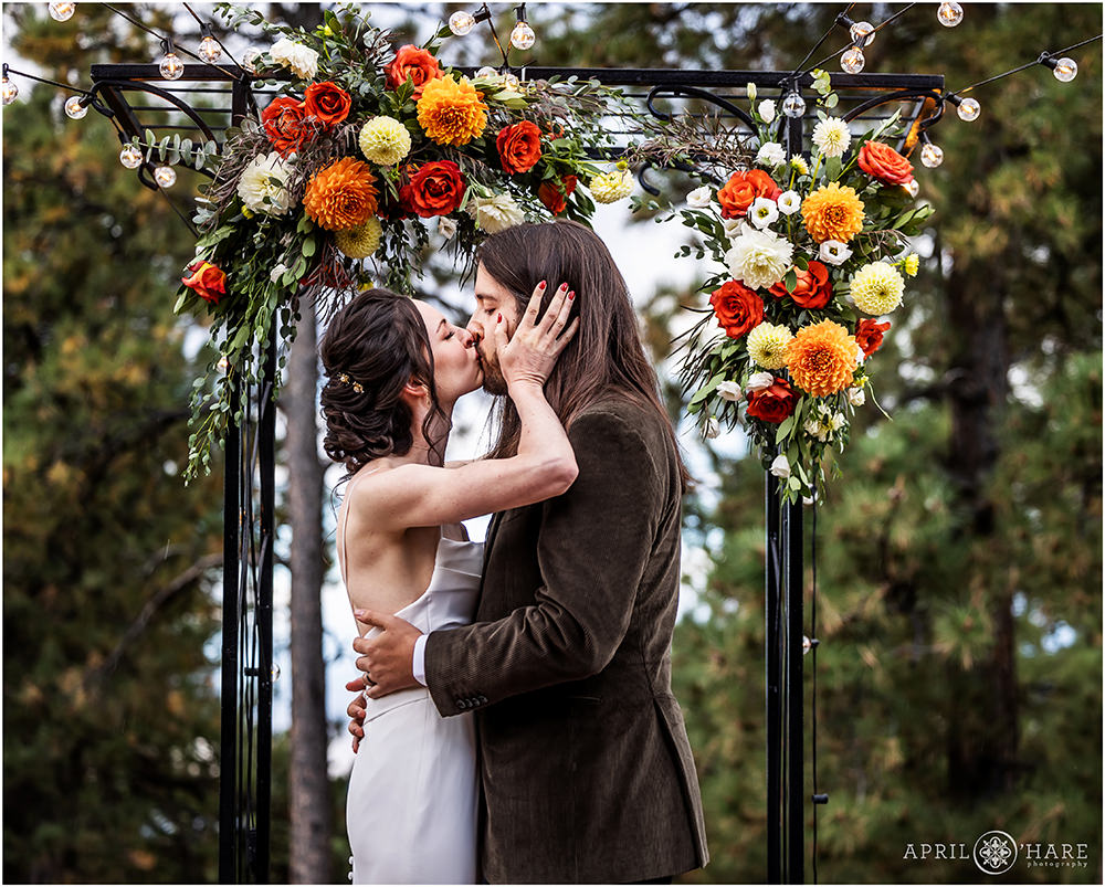 Wedding kiss underneath string lights and orange floral decor at Boettcher Mansion woodsy wedding in Colorado
