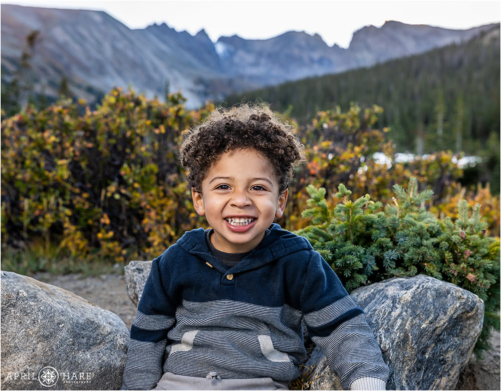 Adorable little boy poses in front of a pretty fall color mountain backdrop at Long Lake in the Indian Peaks Wilderness area of Colorado