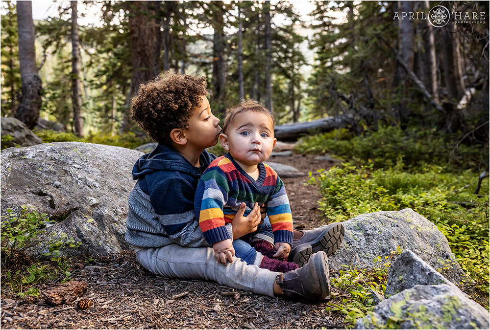 Two young brothers sit on the forest floor on the trail to Long Lake at Indian Peaks Wilderness Area in Colorado