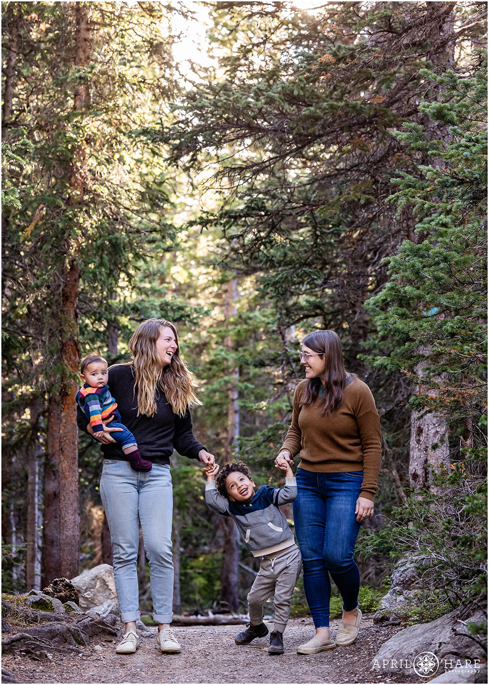 A sweet family of four with two moms walk with their young sons in the woods at Indian Peaks Wilderness Area near Boulder CO