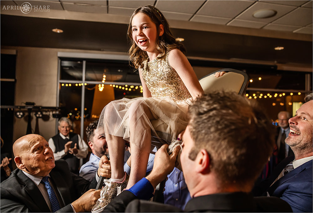 Sister of the bar mitzvah boy sits in the chair during the horah at his party at Curtis Ballroom in Greenwood Village, CO
