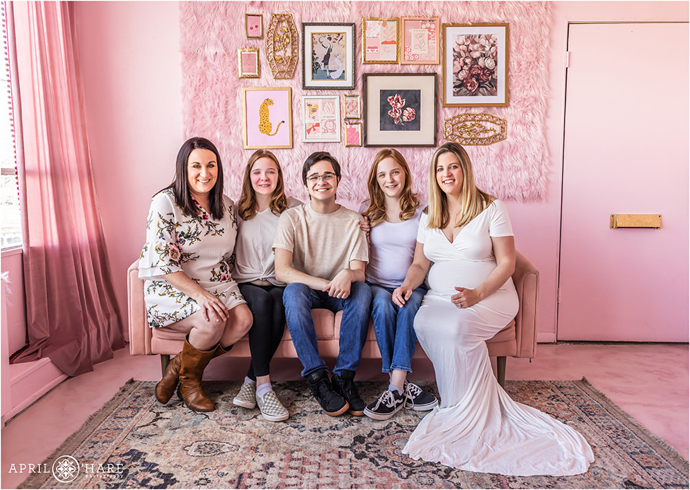 Two moms with their family are photographed for a maternity session family photo in a pretty pink Valentine's Day styled set in Denver