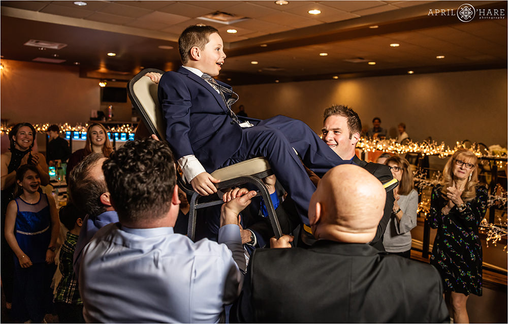 Little brother of the bar mitzvah boy sits in the chair during horah dance at his bar mitzvah party at Curtis Ballroom