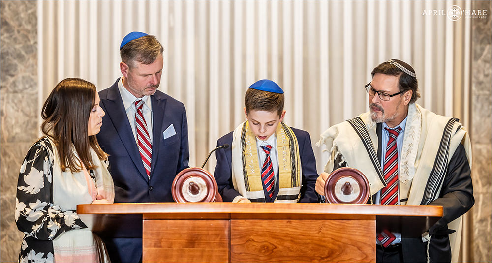 Bar Mitzvah boy reads from the Torah with his parents and his rabbi surrounding him at his rehearsal at Temple Sinai in Denver, CO