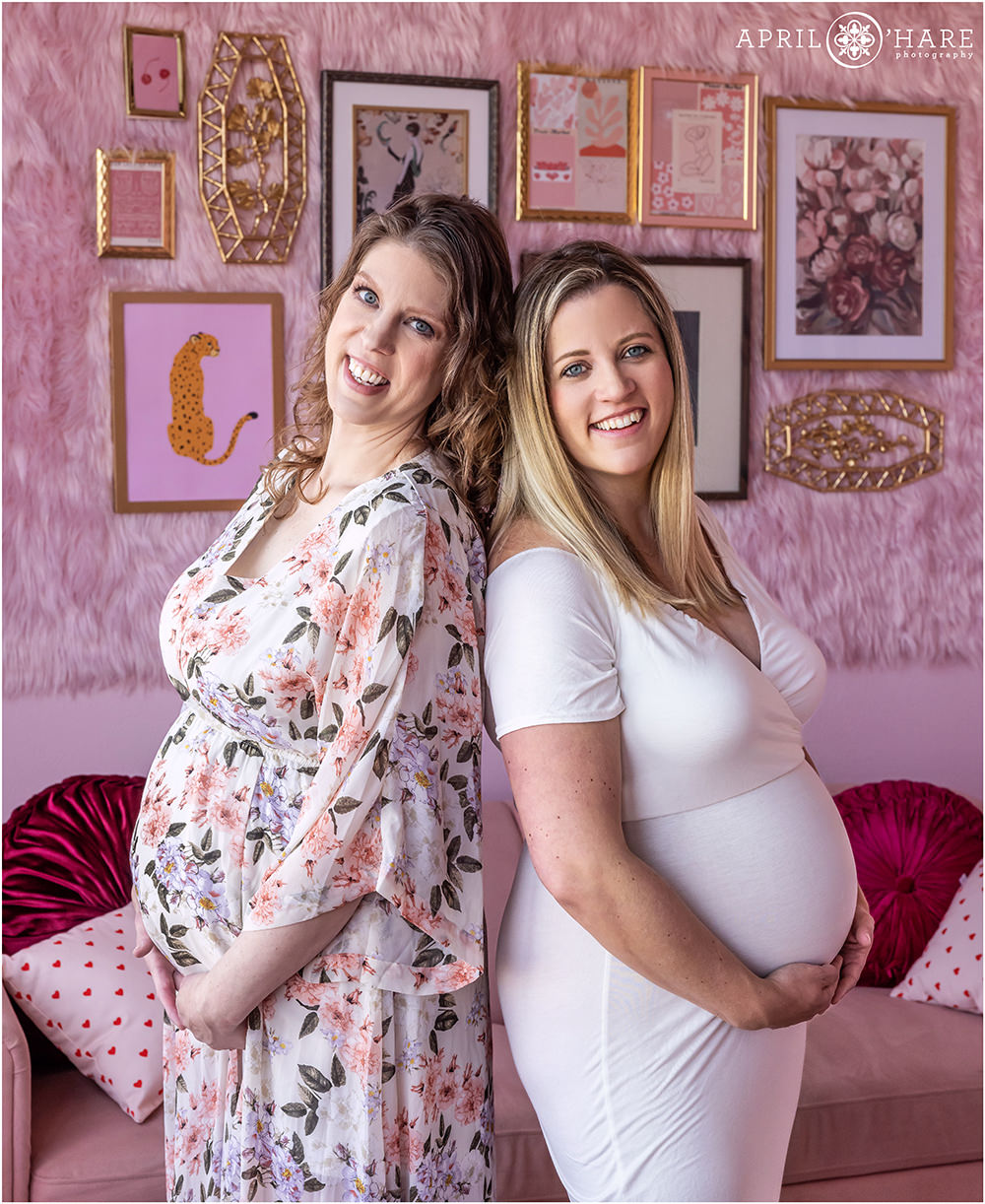 Two pregnant sisters both expecting their first babies two weeks apart are photographed together at their pretty pink Valentine's Day themed maternity session at a styled set at an indoor photography studio in Denver Colorado