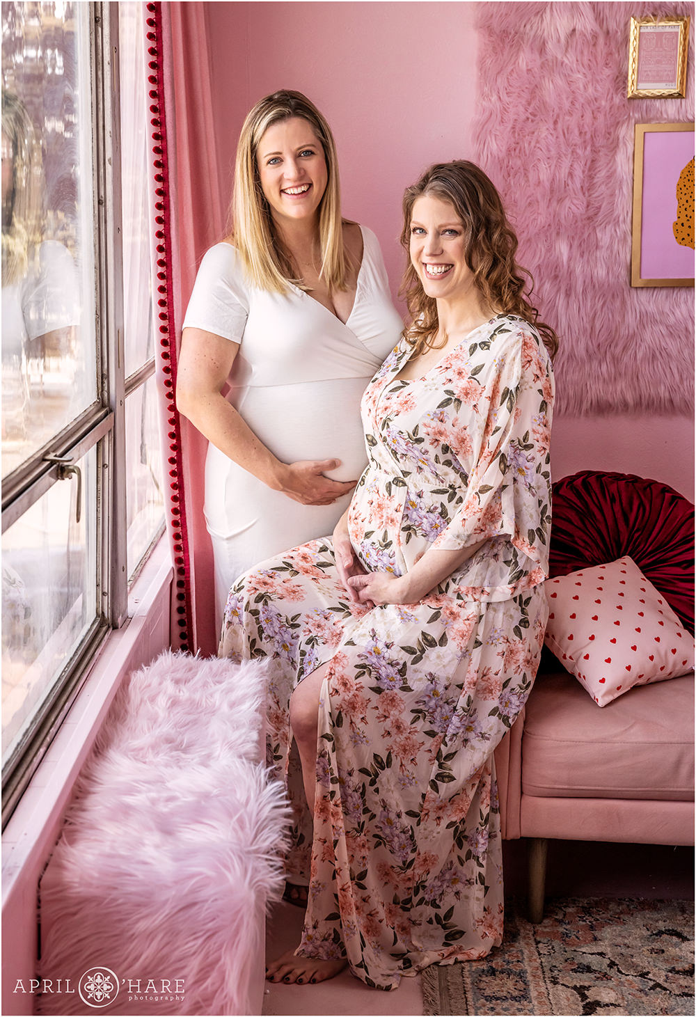 Two sisters pose for a portrait together at their maternity session at a pretty pink Valentine's Day styled indoor studio set in Denver