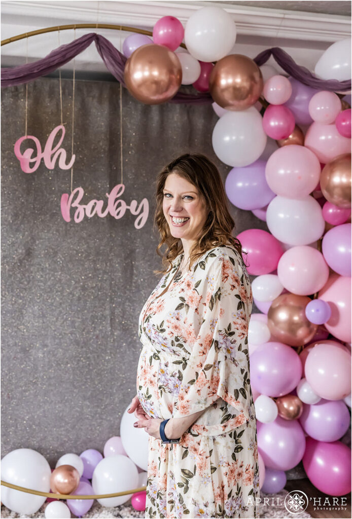 Cute portrait of a pregnant woman holding her belly at her purple and pink baby shower with a balloon arch in Denver