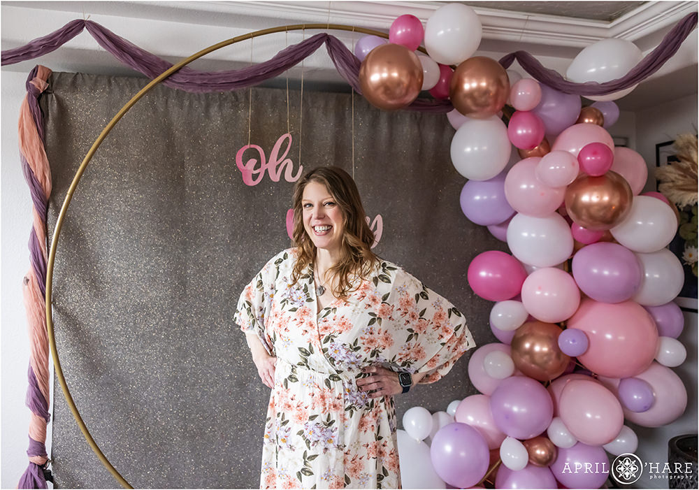 Cute photo of a pregnant woman standing in front of the purple and pink balloon arch at her baby shower in Denver CO