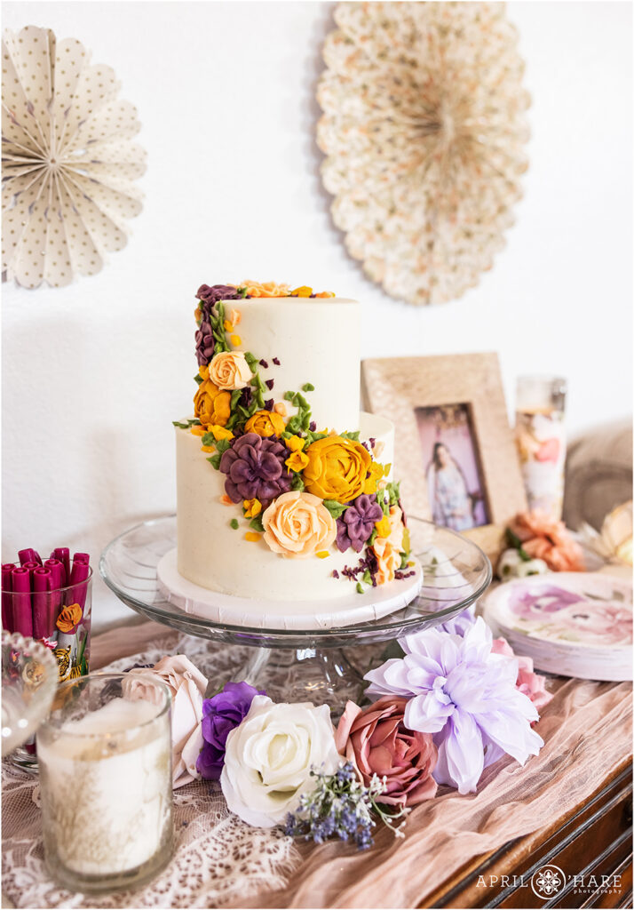 Beautiful detail photo of a two tiered white cake with purple, pink, and yellow floral design at a Denver baby shower