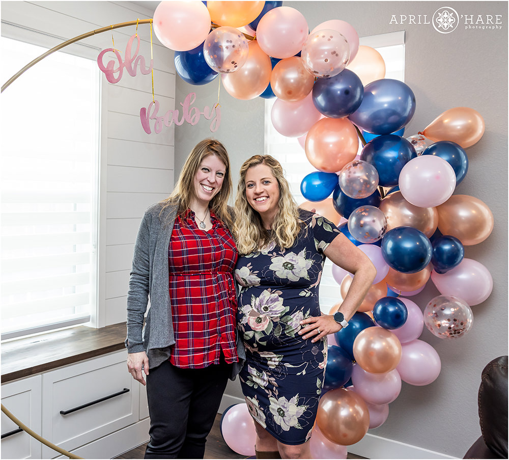 Two pregnant sisters pose together in front of the pretty pink and blue balloon backdrop arch at a Colorado baby shower