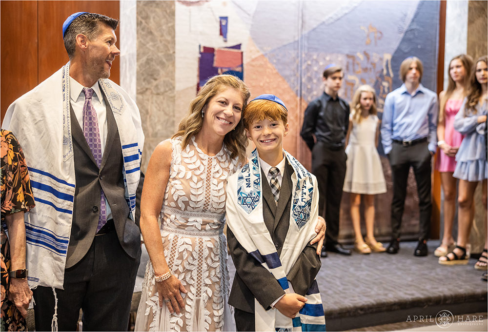 A mother with his son on the day of his bar mitzvah with family nearby at Temple Sinai