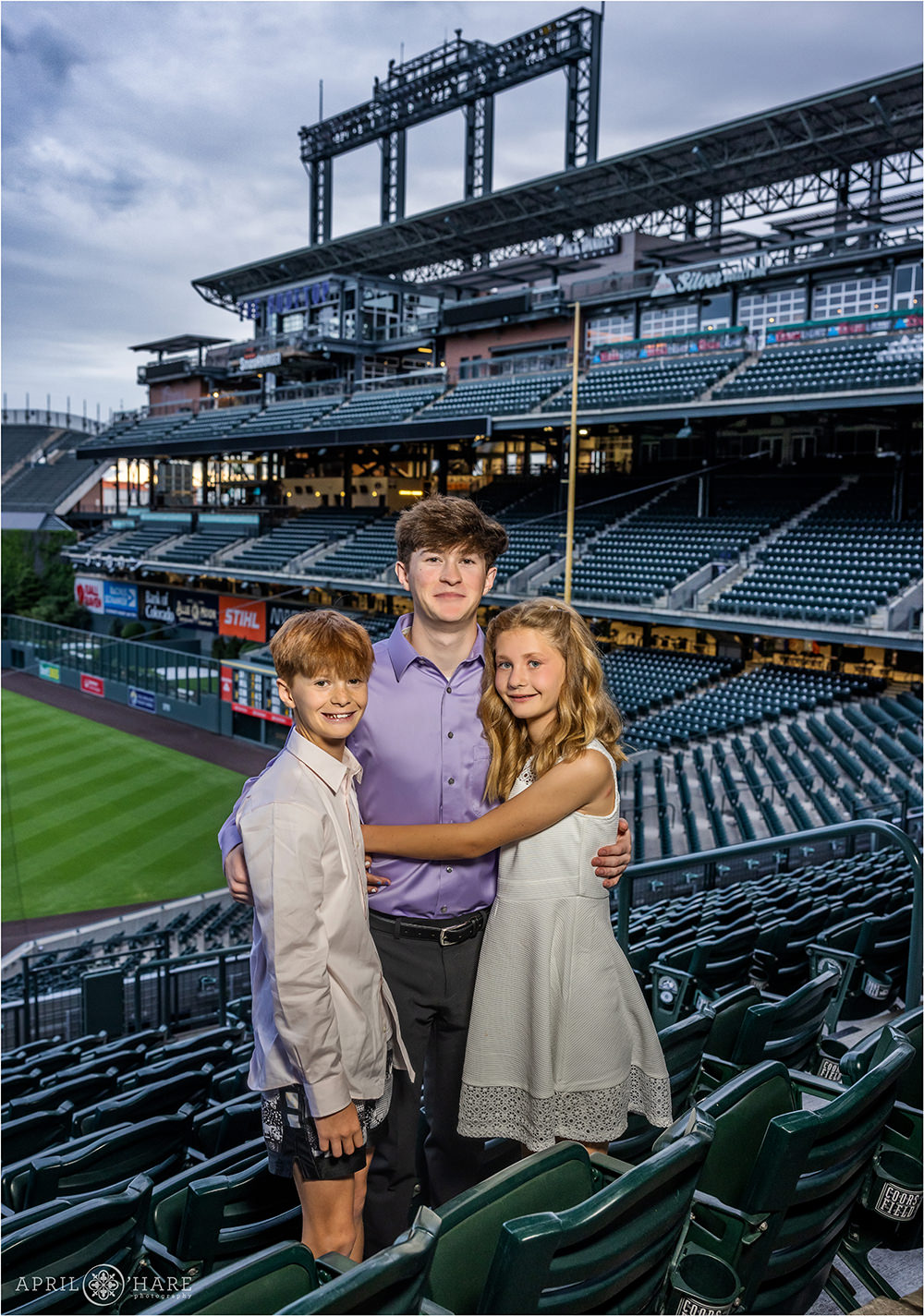 Siblings pose for a sweet photo together with the Coors Field stands in the backdrop at a bar mitzvah party in Denver