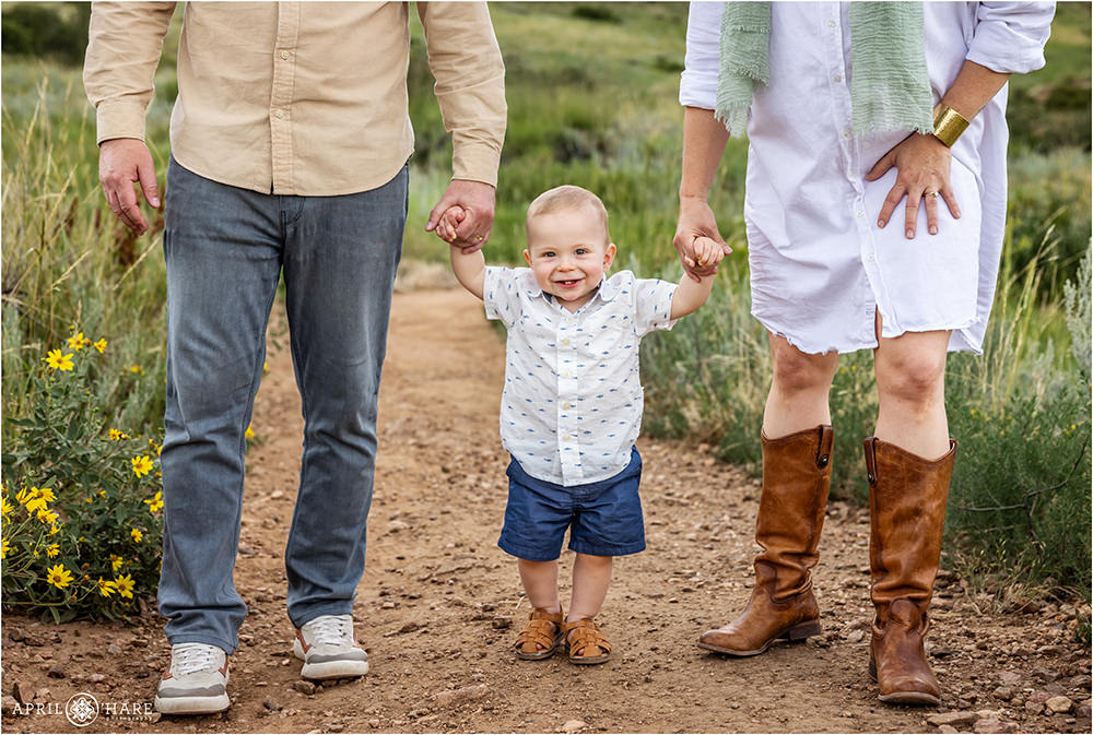 Adorable baby boy holds his parents hands while walking down the path at East Mount Falcon Trailhead in Morrison CO