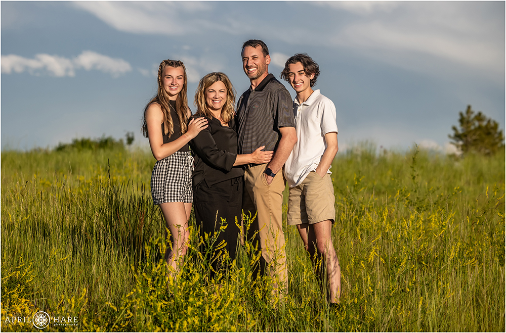 Beautiful family of 4 stand in a field with bright sun lighting their faces in Aurora Colorado
