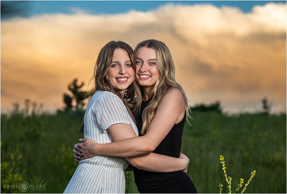 Two sisters hug each other and are photographed at sunset in a pretty field in Aurora Colorado