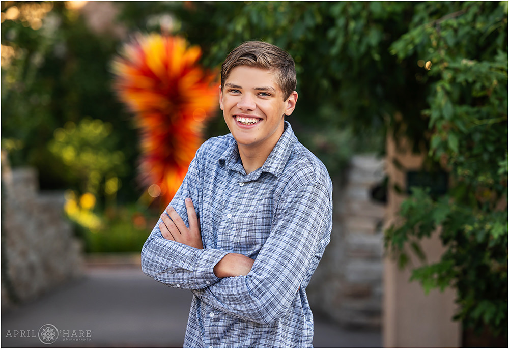 High school senior boy wearing a checkered button down shirt poses for his yearbook photos in front of the Chihuly sculpture at Denver Botanic Gardens during summer