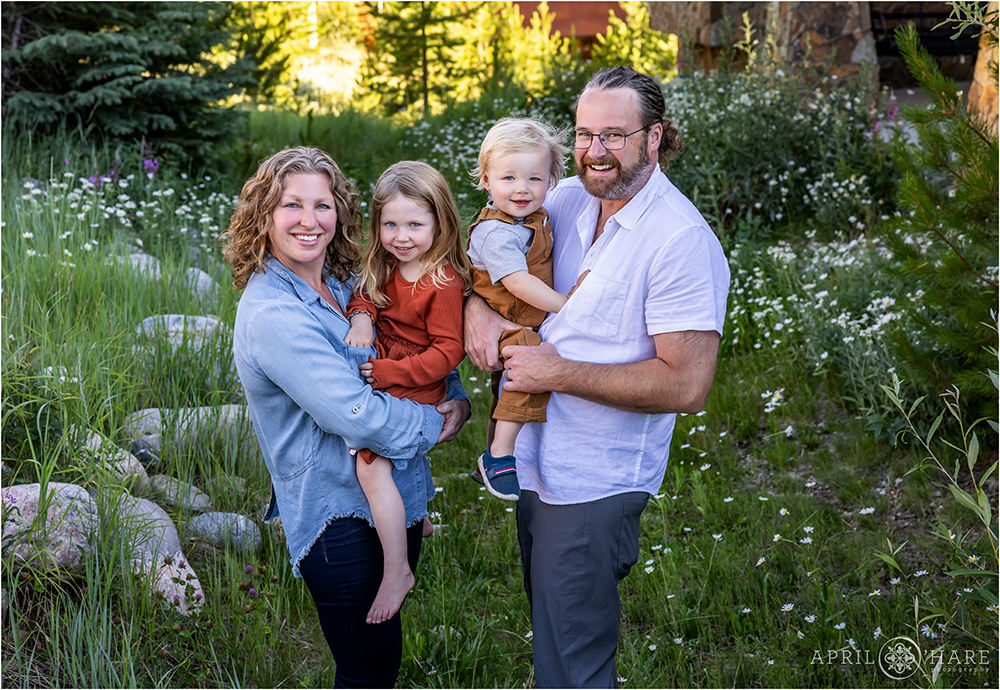 Family of 4 with young children pose in the wildflowers of their Winter Park Colorado mountain home during summer