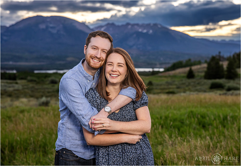 Couple snuggle for a portrait in front of a sunset mountain backdrop near Breckenridge Colorado