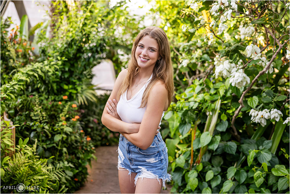 Pretty high school senior girl wearing jean shorts and a white top is photographed in the tropical greenhouse gardens at Denver Botanic Gardens