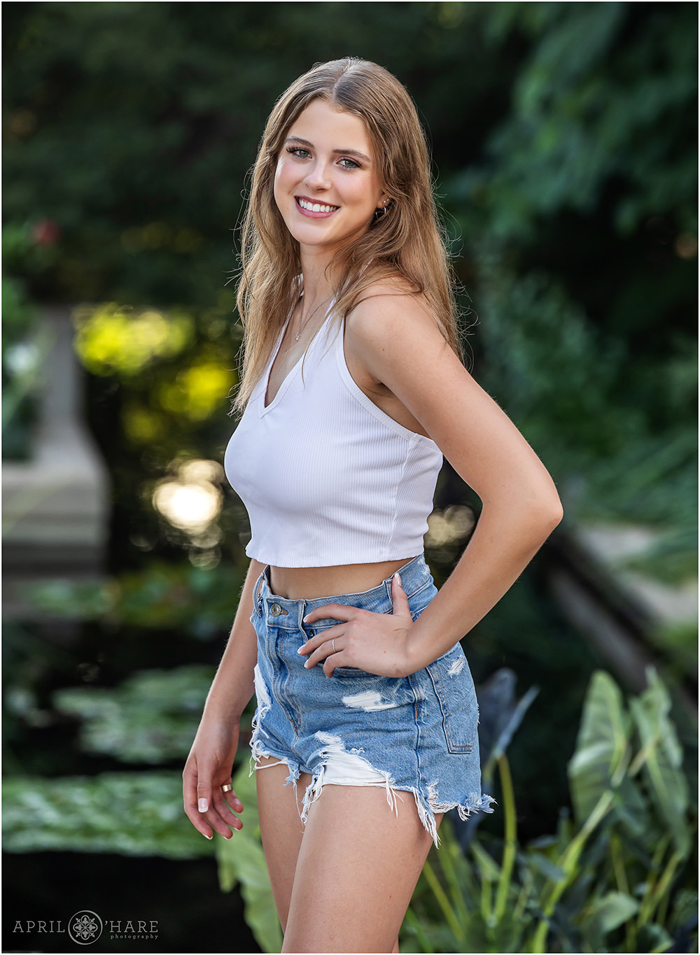 High school senior girl wearing ripped jean shorts with a cute white crop top at her senior photoshoot at Denver Botanic Gardens in Colorado