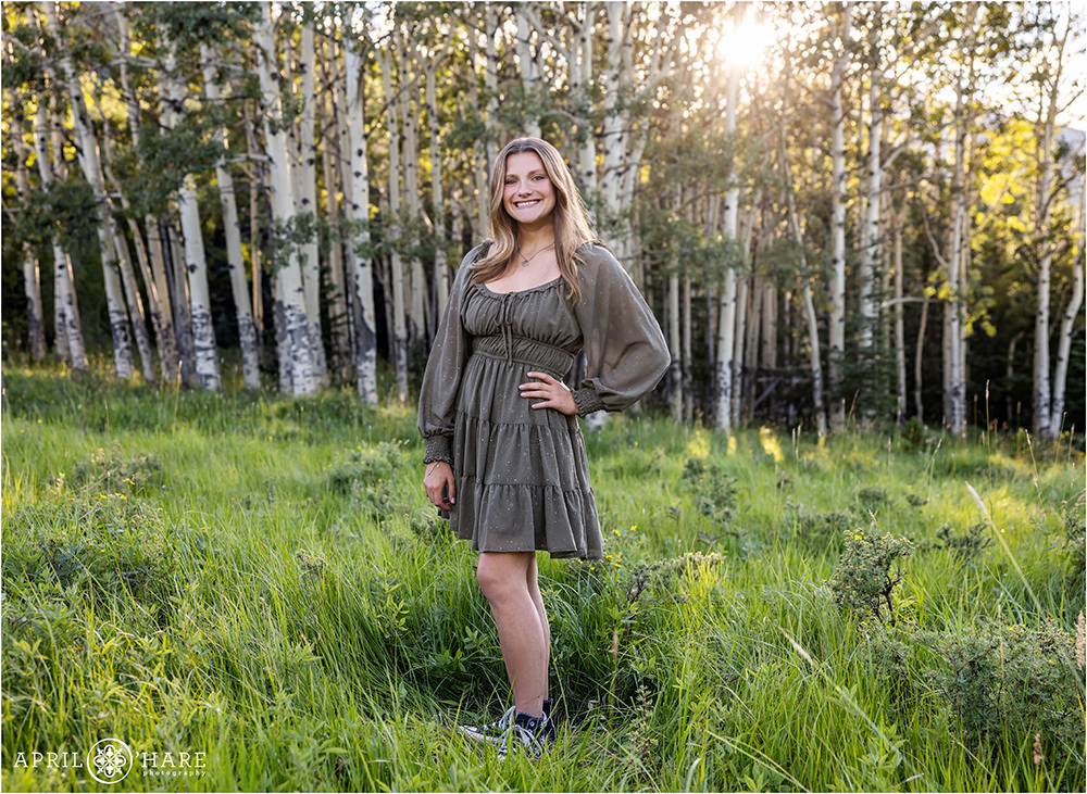 Beautiful girl wearing a fun green dress with gold sparkles on it in a mountain meadow full of aspen trees in Colorado