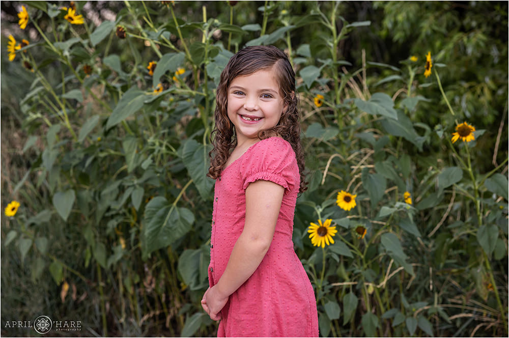 Cute little girl wearing a pink dress standing in front of wild sunflowers in Denver Colorado
