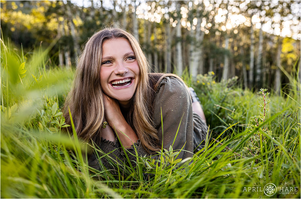 Senior girl laughs as she lies in the mountain meadow on Squaw Pass Road in Evergreen Colorado