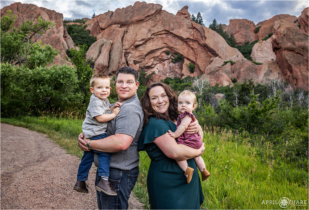Family of four pose for a family picture together in front of a pretty red rocks backdrop at Roxborough State Park