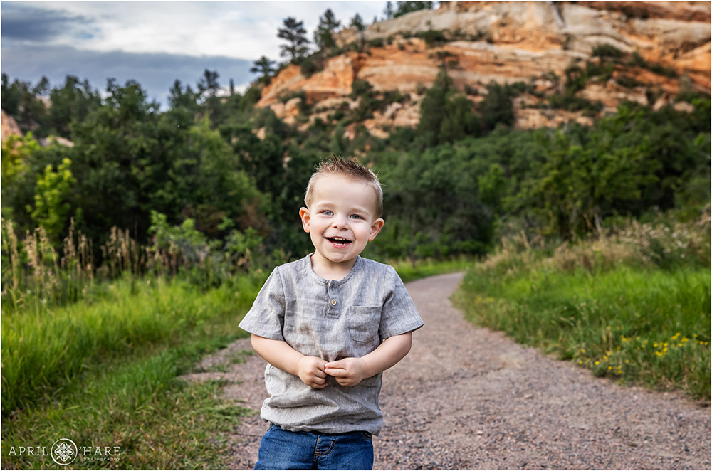 Little boy laughs as he stands on the path at Roxborough State Park in Colorado