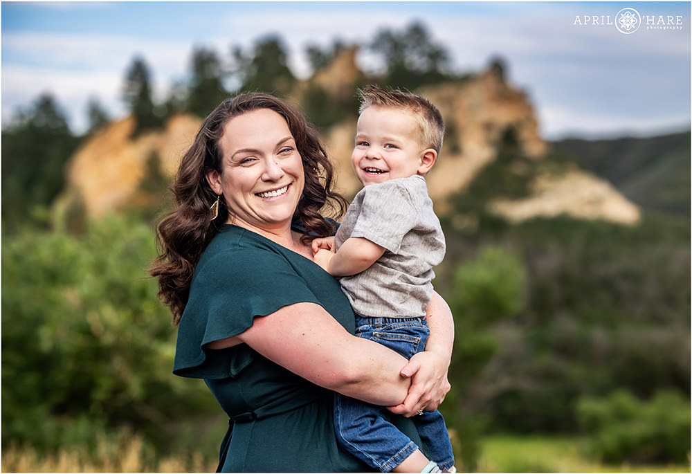 A mom holds her toddler son as they laugh together at their family photoshoot at Roxborough State Park in Colorado