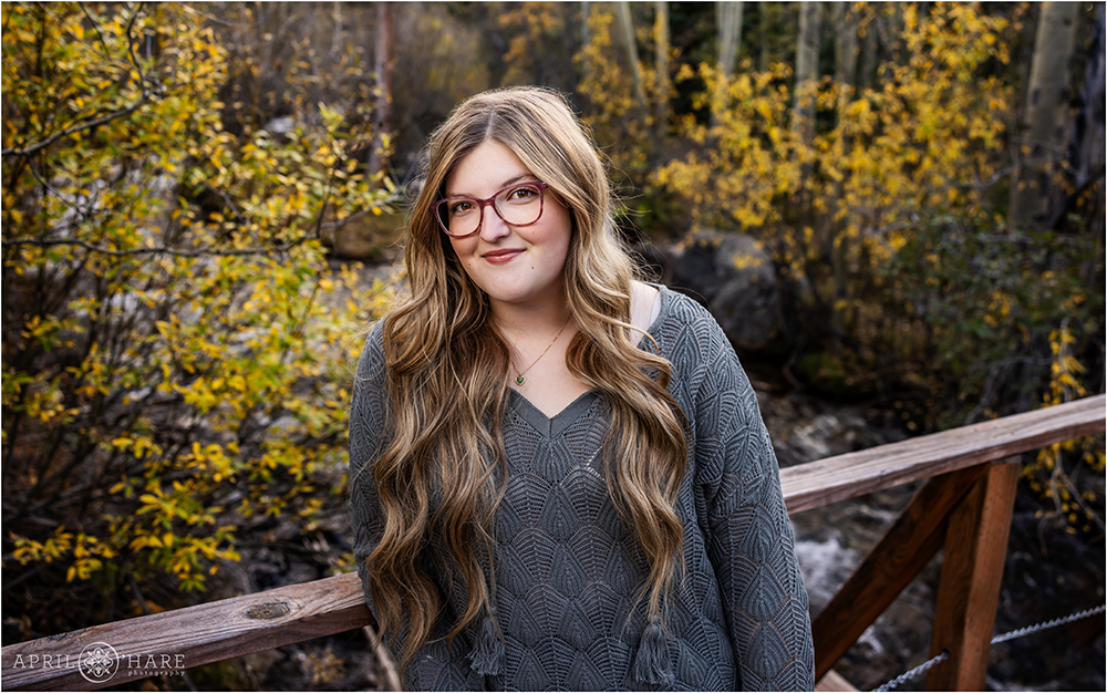 High school senior wearing a gray green sweater poses on a bridge in the fall color on Guanella Pass in Colorado