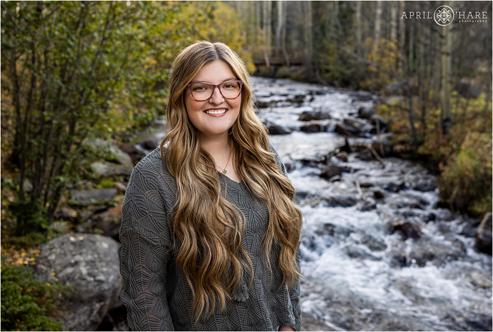 Senior girl with gorgeous long flowing mermaid hair poses in front of a pretty mountain stream with a fall color backdrop on Guanella Pass in Colorado