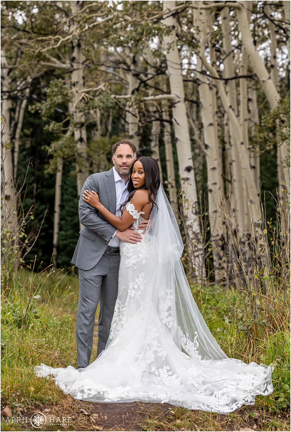 Beautiful bride with her husband wearing a stunning lace wedding gown in the woods with an aspen tree backdrop in Evergreen Colorado