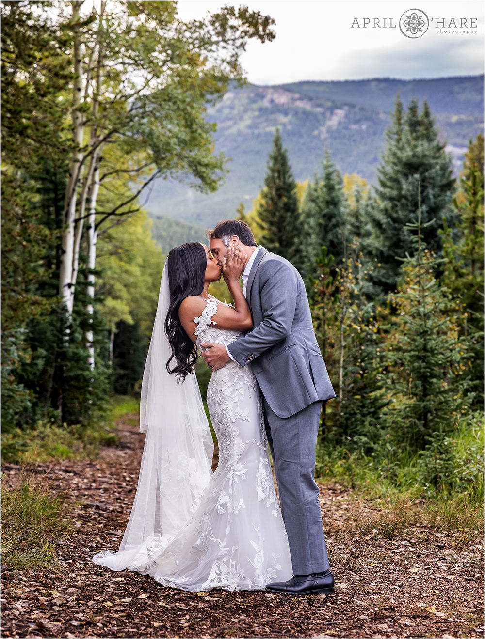 Couple kiss while wearing their beautiful wedding clothes in the woods of Evergreen Colorado