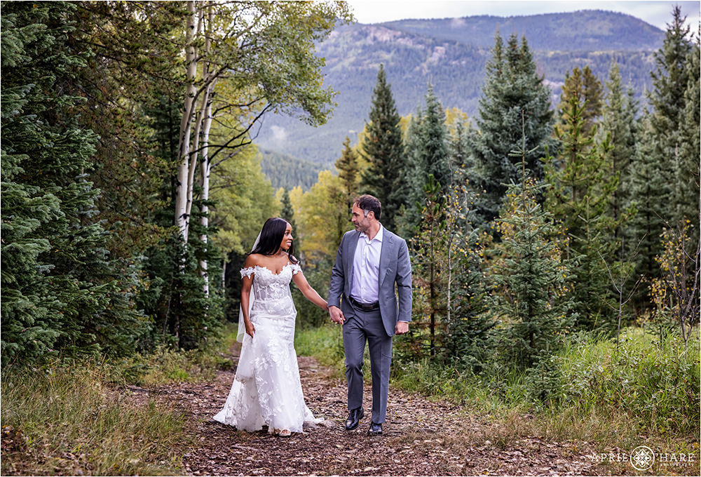 Couple wearing wedding clothes walk along a forest path in the woods of Evergreen Colorado.