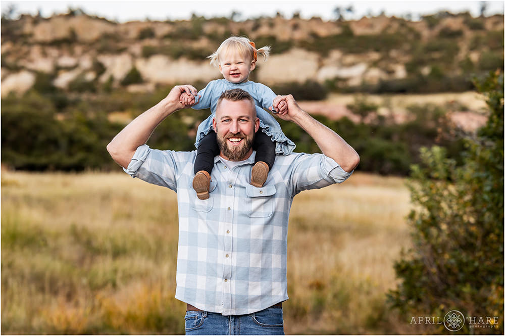 A sweet little girl sits on her daddy's shoulders at their family photography session at South Valley Park in Littleton Colorado