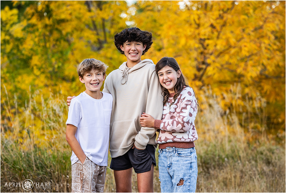 Three siblings pose for a photo together in front of the fall color near their house in Littleton CO