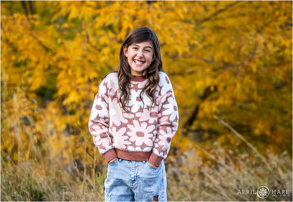 Little girl with pretty brunette hair laughs in front of the fall color near her home in Littleton CO