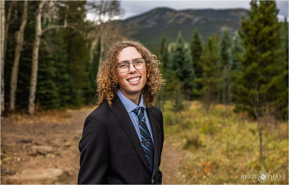 Senior boy wearing a black suit in the woods of Evergreen Colorado